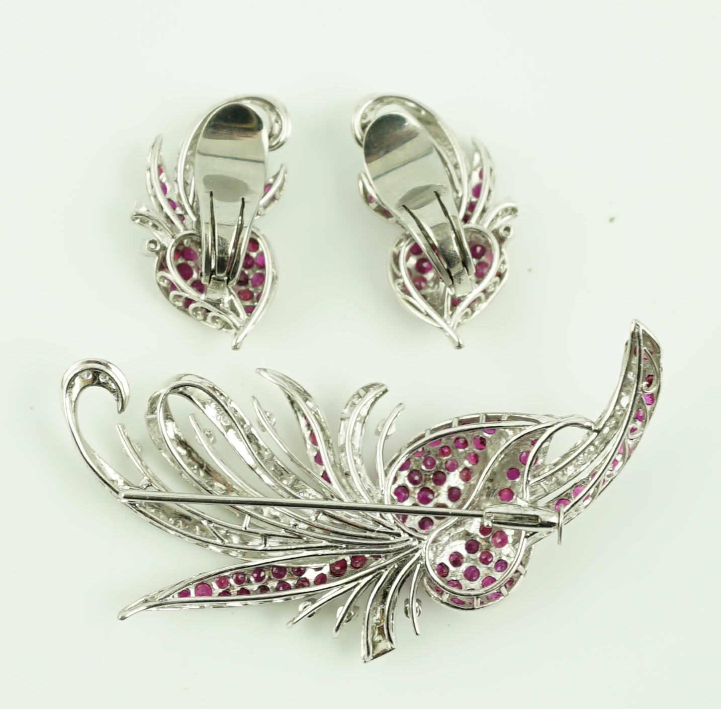 A suite of platinum?, diamond and ruby set cluster jewellery, comprising a spray brooch and pair of matching ear clips